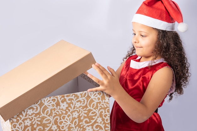 Маленькая бразильская девушка, одетая в рождественский костюм, держит подарочную коробку