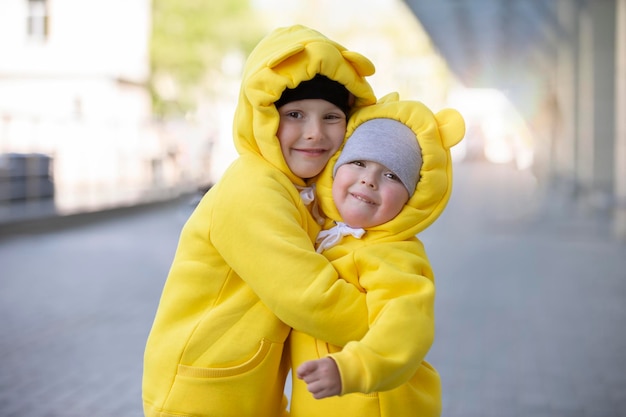 작은 동생과 여동생 재미있는 아이들 노란색 슈트를 입은 소년과 소녀가 서로 포옹합니다