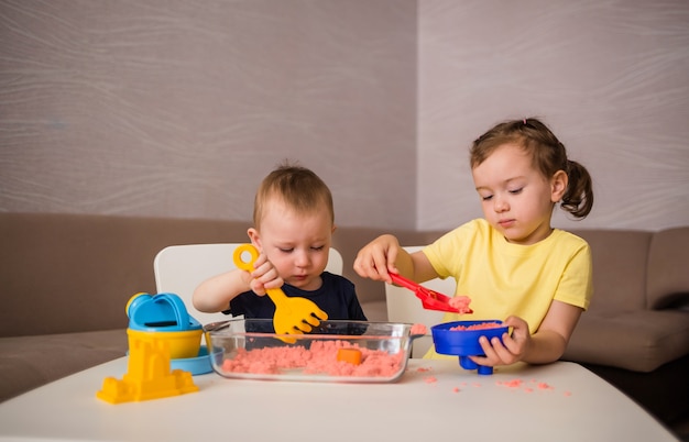 Little brother and sister play in a room with kinetic sand. Children make shapes out of sand.