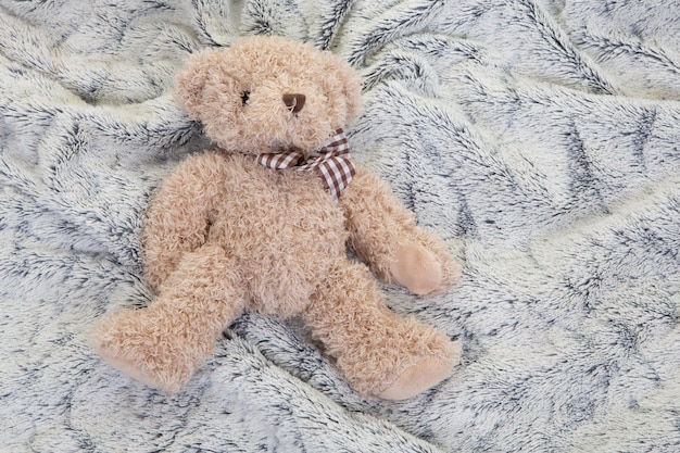 Little brown teddy bear on grey bed baby background