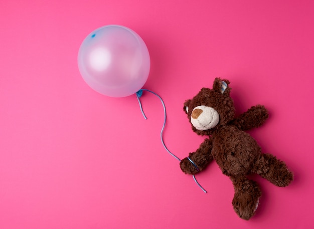 Little brown teddy bear holding a blue inflated balloon