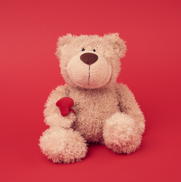 Little brown teddy bear, toy is sitting on a red surface