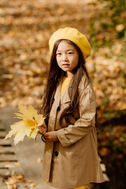 가을 옷을 입은 작은 갈색 머리 아시아 소녀는 개울 근처의 가을 숲에서 산책