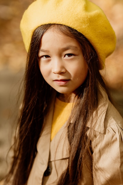 A little brunette Asian girl in autumn clothes walks in the autumn forest near a stream