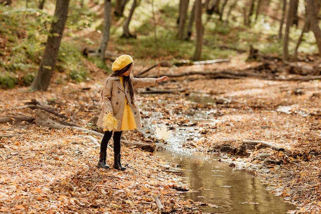 A little brunette Asian girl in autumn clothes walks in the autumn forest near a stream