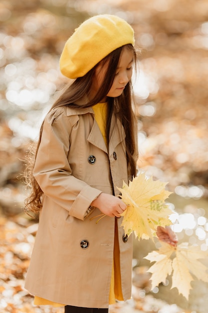 秋の服を着た小さなブルネットのアジアの女の子は、小川の近くの秋の森を歩きます