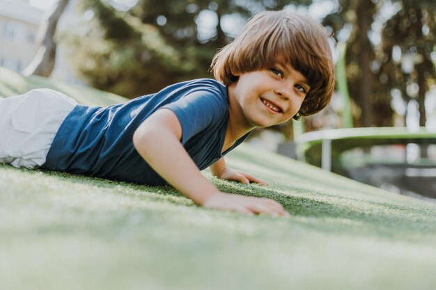 Little brunette boy in a blue T-shirt and white shorts is doing push-ups on a street sports field. child plays and trains outdoors. lifestyle. products for sports and health. space for text