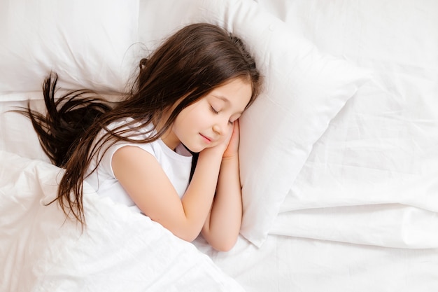 Маленькая брюнетка сладко спит в постели с белым бельем. место для текста. сон здорового ребенка