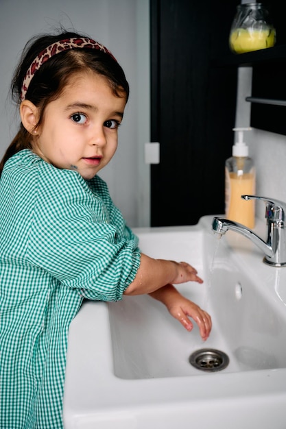 A little brunette girl with a green baby is washing her hands in the bathroom at home