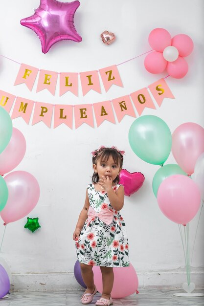 Foto piccola bruna latina circondata da palloncini e con un cartello di buon compleanno sullo sfondo