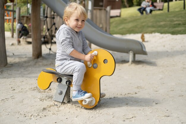 Little caucasian blond boy playing on kids playground in a sunny autumn day.