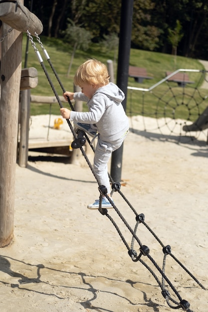 Little caucasian blond boy playing on kids playground in a sunny autumn day.