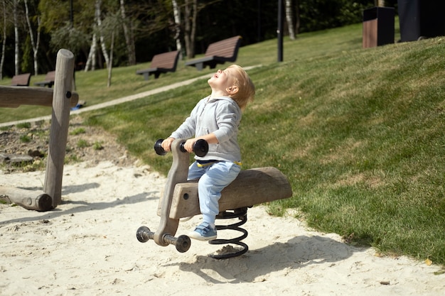 Little caucasian blond boy playing on kids playground in a sunny autumn day.