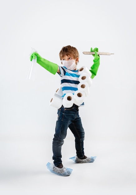 Little caucasian boy as a warrior in fight with coronavirus pandemic, with a face mask, sanitizer, thermometer and toilet paper bandoleer. Teenboy in war for human lives. Concept of childhood, health.