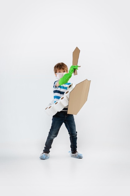 Little caucasian boy as a warrior in fight with coronavirus pandemic, with a shield, a sword and a toilet paper bandoleer. Teenboy in war for human lives. Concept of childhood, health, winning.