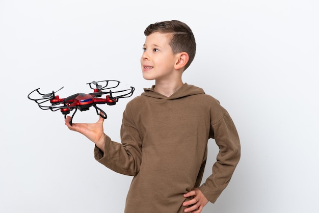 Little Caucasian boy holding a drone isolated on white background looking side