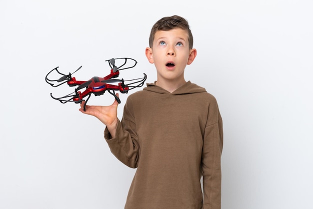 Little Caucasian boy holding a drone isolated on white background looking up and with surprised expression