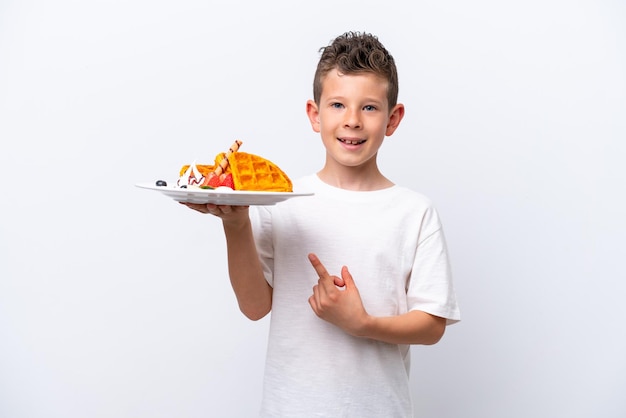 Little caucasian boy holding a waffles isolated on white background and pointing it