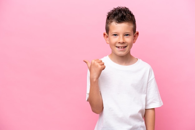 Little caucasian boy isolated on pink background pointing to the side to present a product