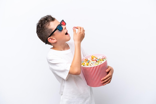 Little caucasian boy isolated on white background with 3d glasses and holding a big bucket of popcorns