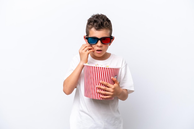 Little caucasian boy isolated on white background with 3d glasses and holding a big bucket of popcorns