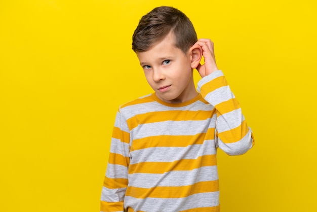 Little caucasian boy isolated on yellow background having doubts