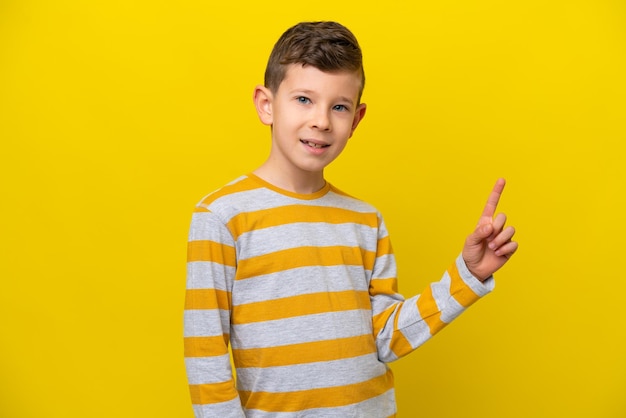 Little caucasian boy isolated on yellow background showing and lifting a finger in sign of the best