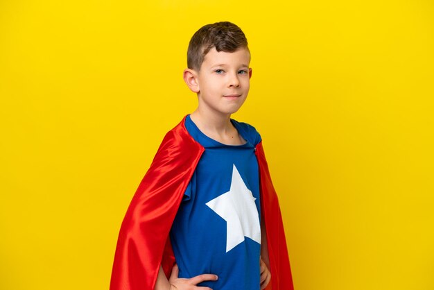 Ragazzino caucasico isolato su sfondo giallo in costume da supereroe con le braccia incrociate