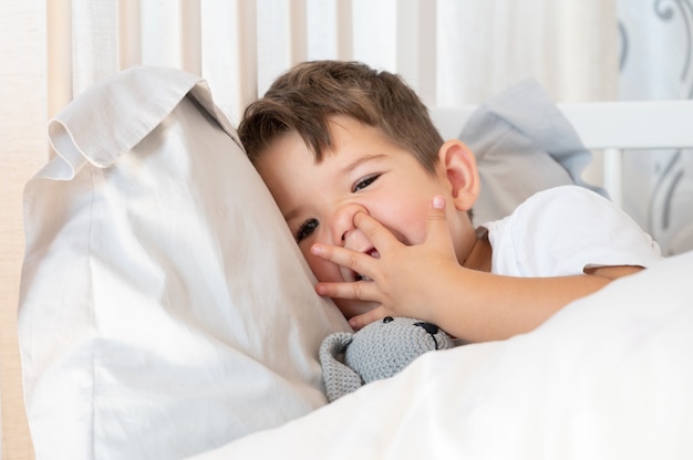 Маленький кавказский мальчик ковыряется в носу. Мальчик нежится в своей постели.