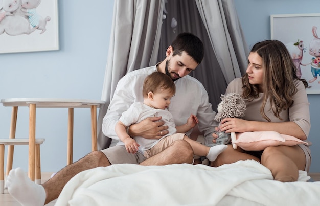 Piccolo ragazzo caucasico che gioca con i suoi genitori amorevoli famiglia caucasica felice seduta su un comodo divano nella moderna camera dei bambini