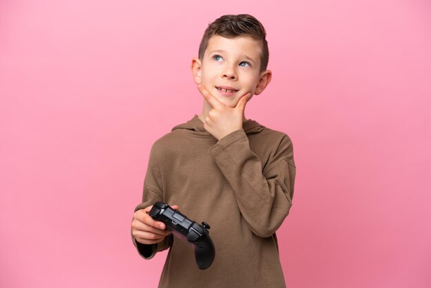 横を見て笑っているピンクの背景に分離されたビデオゲームコントローラーで遊んでいる小さな白人の少年