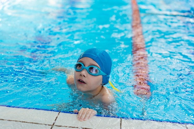 Little caucasian boy wearing goggles looking out from swimming pool