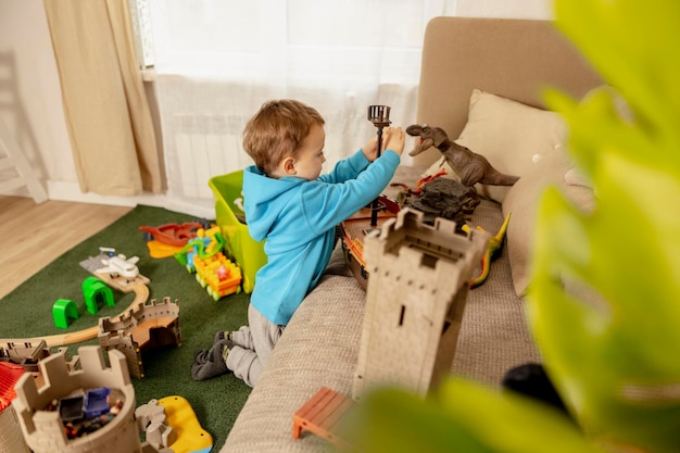 Little caucasian boy with blue hoodie playing with colourful toys at home Child having fun Happy and cheerful kid plays with ship dinosaurs castle Leisure activity domestic life Cozy room