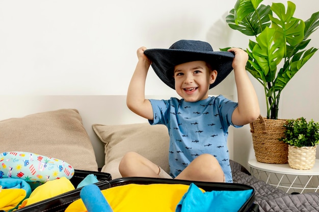 Little caucasian boy with blue shirt ready for vacation Happy child packs clothes into a suitcase for travel Tourist joy of holiday Kid at home preparing for flying Modern and cozy interior