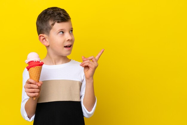 Little caucasian boy with a cornet ice cream isolated on yellow background intending to realizes the solution while lifting a finger up