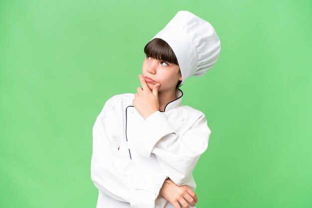 Little caucasian chef girl over isolated background having doubts and with confuse face expression