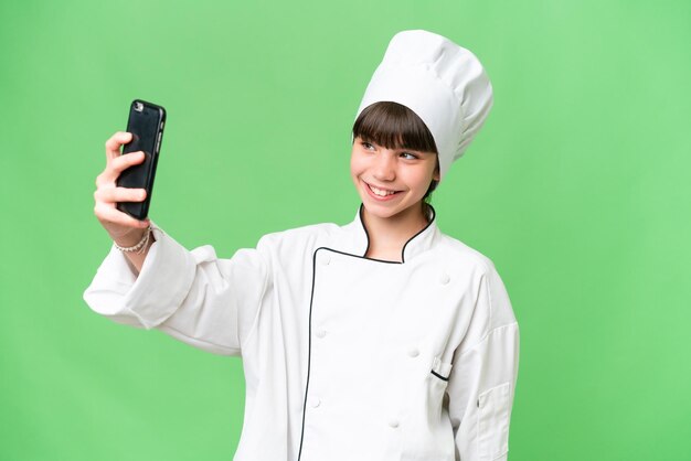 Little caucasian chef girl over isolated background making a selfie