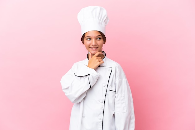 Little caucasian chef girl isolated on pink background looking to the side