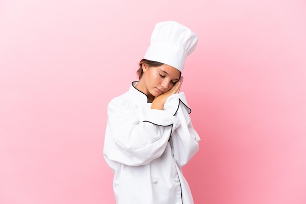 Little caucasian chef girl isolated on pink background making sleep gesture in dorable expression