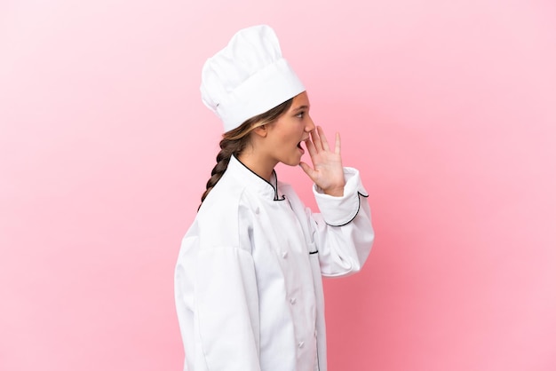 Little caucasian chef girl isolated on pink background shouting with mouth wide open to the lateral