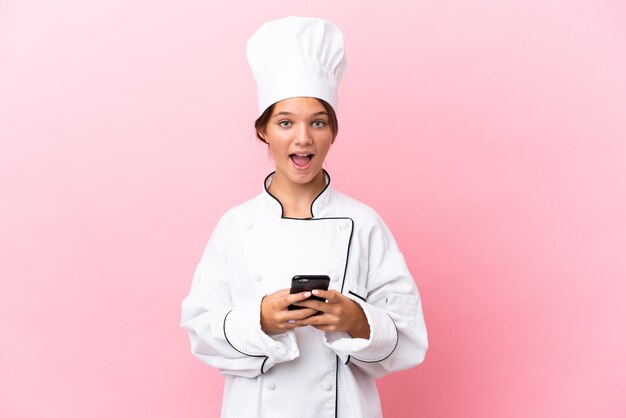 Little caucasian chef girl isolated on pink background surprised and sending a message