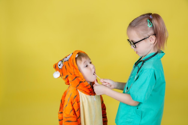 I piccoli bambini caucasici giocano al dottore, il ragazzo in costume da tigre mostra la gola al pediatra all'appuntamento del medico