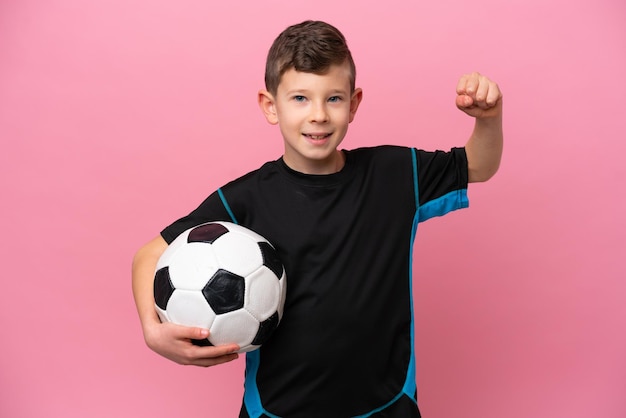 Little caucasian football player boy isolated on pink background celebrating a victory