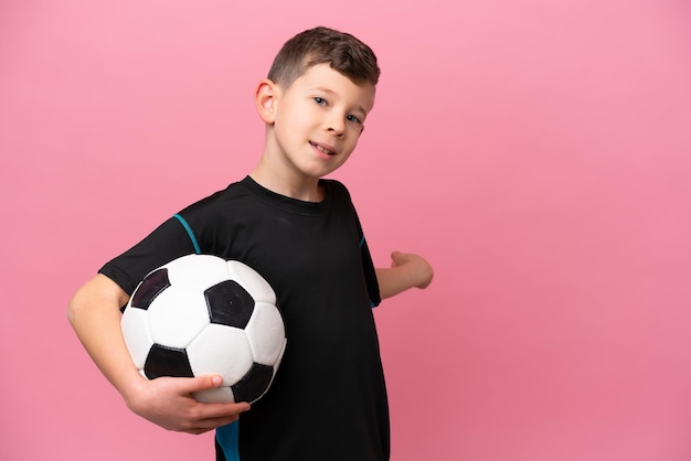 Little caucasian football player boy isolated on pink\
background extending hands to the side for inviting to come