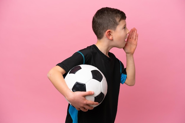 Little caucasian football player boy isolated on pink\
background shouting with mouth wide open to the side