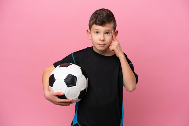 Piccolo ragazzo caucasico del giocatore di football isolato su fondo rosa che pensa un'idea