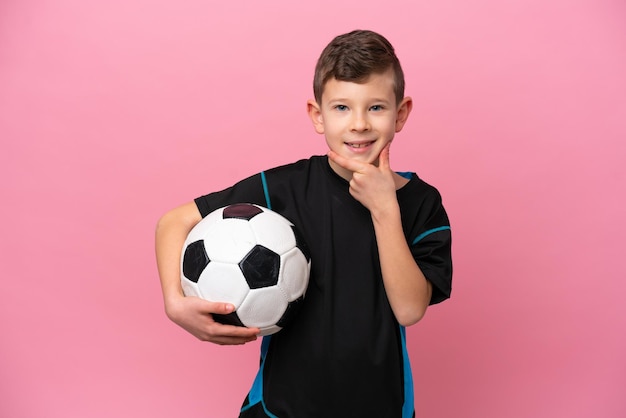 Little caucasian football player boy isolated on pink background thinking