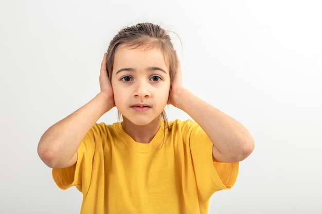 Little caucasian girl covered her ears on a white background isolated