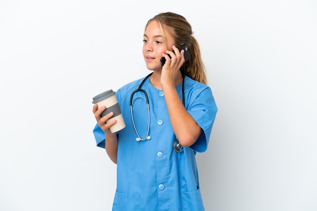 Little caucasian girl disguised as surgeon isolated on white background holding coffee to take away and a mobile