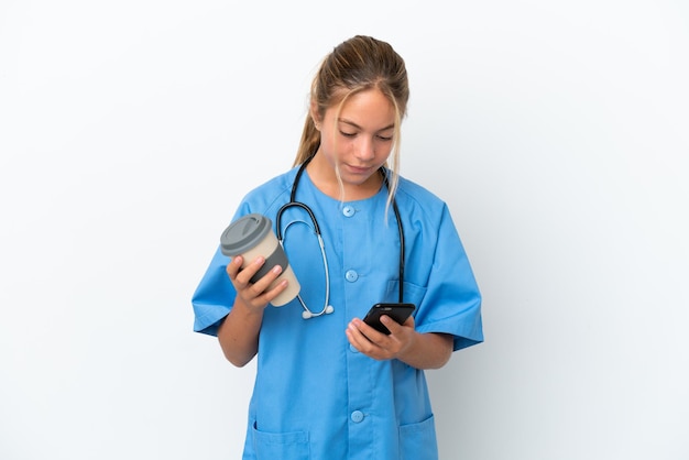 Little caucasian girl disguised as surgeon isolated on white background holding coffee to take away and a mobile